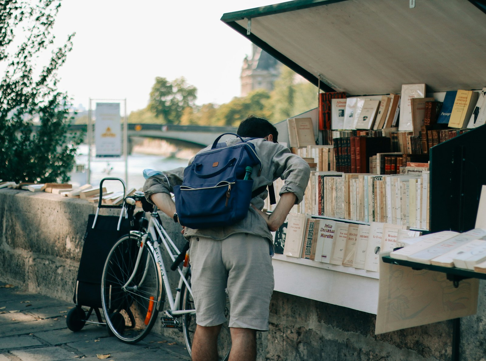 man in blue jacket and gray pants with blue backpack standing beside bicycle during daytime