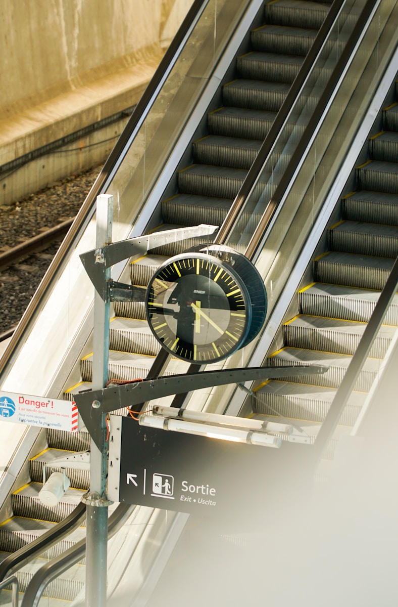 A clock hangs near escalators at a train station.